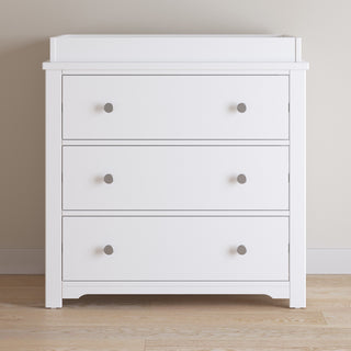 The Child Craft Harmony 3-Drawer Dresser with Changing Table Topper in matte white features a modern design with clean lines and round silver handles, making it perfect for nursery storage or use as a changing station.