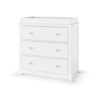 The Child Craft Harmony 3-Drawer Dresser with Changing Table Topper in matte white features three drawers with round silver knobs, clean lines, a raised top edge, and short legs—ideal for nursery storage or use as a changing table.