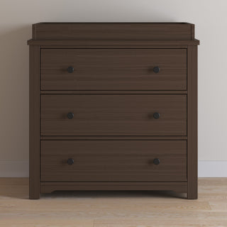 The Child Craft Harmony 3-Drawer Dresser with Changing Table Topper in Brushed Truffle stands against a light-colored wall on a light wood floor.