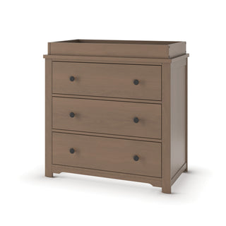 The Child Craft Harmony 3-Drawer Dresser with Changing Table Topper in Dusty Heather features a raised edge top, round black handles, and short legs, shown against a plain white background.