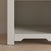 A close-up of the bottom section of the Child Craft Harmony Nightstand in Brushed Cotton on a wood floor against a beige wall. The empty nightstand features a small decorative cutout at its base.