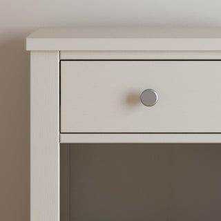 Close-up of the Harmony Nightstand in Brushed Cotton by Child Craft, highlighting the top left corner with a single drawer featuring a round silver knob and an open shelf below, set against a plain light-colored wall.