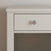 Close-up of the Harmony Nightstand in Brushed Cotton by Child Craft, highlighting the top left corner with a single drawer featuring a round silver knob and an open shelf below, set against a plain light-colored wall.