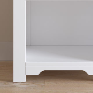 A close-up of the Child Craft Harmony Nightstand, Matte White, shows the open-front bottom shelf with child-safe finishes—ideal for bedside storage—on a light wood floor against a beige wall.