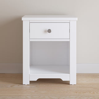 The Child Craft Harmony Nightstand in Matte White features child-safe finishes, a single drawer with a silver knob, and an open lower shelf for storage, offering a clean, modern look.