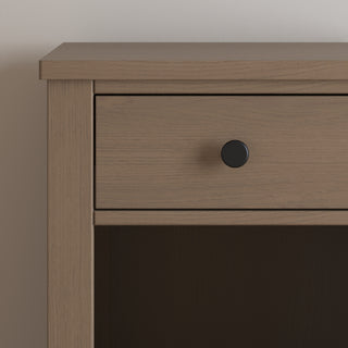 A close-up of the Child Craft Harmony Nightstand in Dusty Heather reveals a single drawer with a round black knob, practical bedside storage, light brown wood grain, and child-safe finishes for added peace of mind.