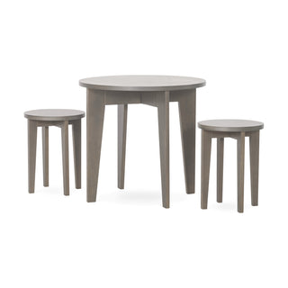 The Child Craft Geo Table and Stools Set in Dapper Gray features a round, light gray wooden table with three legs and two matching four-legged round stools, all displayed against a plain white background.