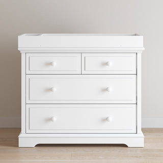 The Child Craft F01792 Universal Changing Table Topper in Matte White is ideal for pairing with a four-drawer white wooden dresser, creating a practical nursery setup against any plain wall.