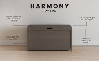 The Child Craft Harmony 33" Kids Toy Box in Dapper Gray features a bench seat supporting up to 300 lbs, spacious storage, standard ventilation holes, and two safety hinges for soft closing. Shown against a plain wall and wooden floor.