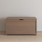 The Child Craft Harmony 33" Kids Toy Box in Dusty Heather features a flat lid with a small handle cutout, shown against a light-colored wall on a wooden floor.