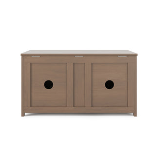 The Child Craft Harmony 33" Kids Toy Box in Dusty Heather features a flat-top wooden bench with two panel doors, each with a circular cut-out handle. Its simple, modern design comes in a light brown finish.