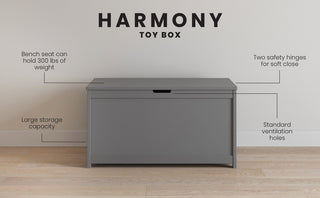 The Child Craft Harmony 33" Kids Toy Box in Cool Gray sits against a wall, featuring a bench seat supporting 300 lbs, roomy storage, two soft-close safety hinges, and standard ventilation holes.