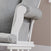 Close-up of the Child Craft Cozy Glider and Ottoman in Matte White, featuring light gray cushions, rolled armrest with side pocket, white wooden supports, and partial seat view against a beige wall.