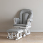 The Child Craft Cozy Glider and Ottoman, Matte White, features plush gray cushions and white wooden frames. Both pieces sit on a wooden floor against a simple light wall.