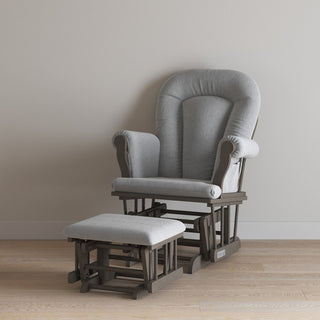 The Child Craft Cozy Glider and Ottoman in Dapper Gray, featuring dark wooden frames, sits on a light wood floor against a plain beige wall.