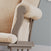 Close-up of the Child Craft Cozy Glider and Ottoman in Dusty Heather, featuring a beige cushion, wooden armrest, and side pocket, set against a light blue wall.
