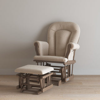 The Child Craft Cozy Glider and Ottoman in Dusty Heather, featuring a cushioned seat and wooden frame, is placed on a light wood floor against a plain, light-colored wall.