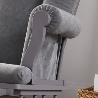 A close-up of the Child Craft Cozy Glider and Ottoman in Cool Gray, featuring padded armrests and a side pocket, sits beside a woven basket on a light-colored floor.