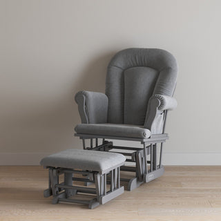 The Child Craft Cozy Glider and Ottoman in Cool Gray, with padded armrests and a matching ottoman, sits on a light wood floor against a beige wall, making it a cozy nursery chair option.