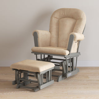 The Child Craft Tranquil Nursery Glider Cushion, in beige with gray wood frames, rests on a light wood floor against an off-white wall.