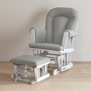 The Child Craft Tranquil Nursery Glider and Ottoman in matte white with gray cushions sits on a light wood floor against a plain beige wall.