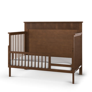 The Child Craft F09502 Toddler Guard Rail in Cocoa Bean is a wooden bed with three closed slatted sides, one open side with a guard rail, and a low white mattress—ideal for an easy transition from a Child Craft crib.
