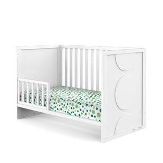 The Child Craft F09501 Toddler Guard Rail in Matte White offers sturdy wood construction with side rails and a toddler guard rail. The headboard features large circular designs, and the mattress is dressed in green and blue polka dot sheets.