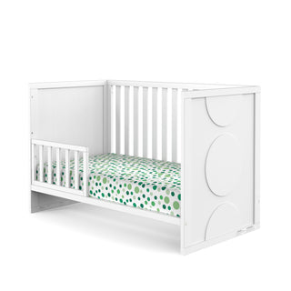 The Child Craft F09501 Toddler Guard Rail in Matte White offers sturdy wood construction with side rails and a toddler guard rail. The headboard features large circular designs, and the mattress is dressed in green and blue polka dot sheets.