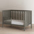 The Child Craft F09501 Toddler Guard Rail in Lunar Gray, featuring strong wood construction and slatted sides, is shown on a light wood floor against a plain beige wall.