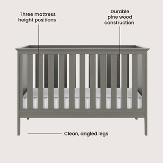 The Child Craft Atwood 3-in-1 Euro Convertible Crib in Lunar Gray features vertical slats, three mattress height positions, clean angled legs, and durable pine wood construction. Labels highlight each feature.