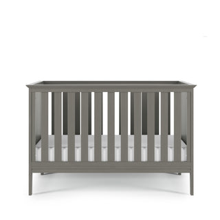 The Child Craft Atwood 3-in-1 Euro Convertible Crib in Lunar Gray features vertical slats on all sides and comes with a white mattress, shown against a plain white background.