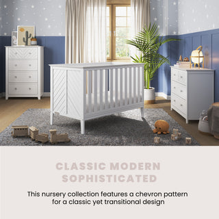 A modern nursery with the Child Craft Atwood 3-in-1 Euro Convertible Crib in matte white, coordinating dressers, toys on a gray rug, blue and white walls, beige-curtained window, star wallpaper. Described as Classic Modern Sophisticated.