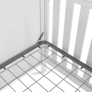 Close-up of the Child Craft Atwood 3-in-1 Euro Convertible Crib in Matte White, showing its metal bed frame with wire mesh base attached to white slatted panels, focusing on the corner and support brackets.