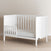 The Child Craft Atwood 3-in-1 Euro Convertible Crib in Matte White features slatted sides and a partial guardrail, shown in a room with light walls and wood flooring.