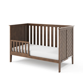 The Child Craft F09501 Toddler Guard Rail in Cocoa Bean features a partial guard rail, vertical slats, and a chevron-patterned panel—ideal for smooth crib-to-toddler bed conversion with Child Craft cribs.
