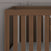 A close-up view of the Child Craft Kieran 3-in-1 Convertible Crib in Toasted Chestnut, featuring vertical slats and a gray mattress, set against a gray paneled wall.