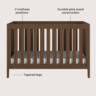 The Child Craft Kieran 3-in-1 Convertible Crib in Toasted Chestnut features vertical slats, tapered legs, a white mattress, two adjustable mattress positions, and durable pine wood construction.