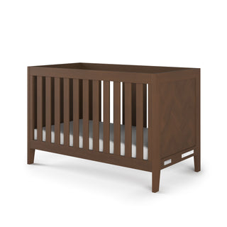 The Child Craft Kieran 3-in-1 Convertible Crib in Toasted Chestnut features vertical side slats and includes a white mattress, displayed against a plain white background.