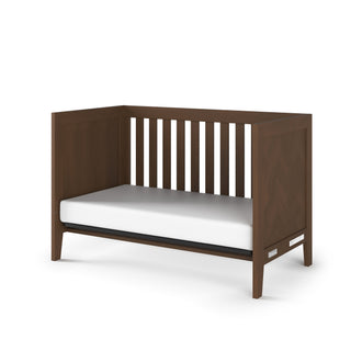 The Child Craft Kieran 3-in-1 Convertible Crib in Toasted Chestnut features an open front, slatted sides, white mattress, and a modern minimalist design with clean lines and sturdy construction.