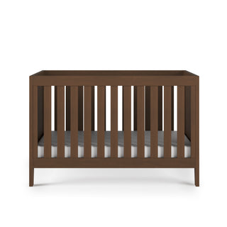 The Child Craft Kieran 3-in-1 Convertible Crib in Toasted Chestnut features vertical slats on all sides and comes with a white mattress, displayed against a plain white background.
