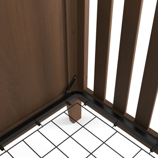 Close-up of the inside corner of the Child Craft Kieran 3-in-1 Convertible Crib in Toasted Chestnut, showing the metal mattress support frame secured to the sides and a grid of metal wires forming the mattress base.
