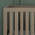 A close-up of the Kieran 3-in-1 Convertible Crib in Crescent Gray by Child Craft, featuring vertical wooden slats, set against a textured green wall.