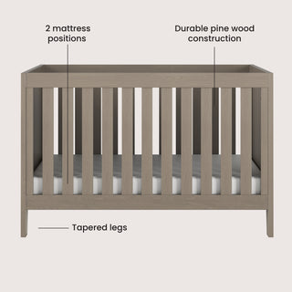 The Kieran 3-in-1 Convertible Crib by Child Craft in Crescent Gray features vertical slats, 2 mattress positions, durable pine wood construction, and tapered legs, with black text and lines highlighting each feature.