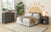 A modern bedroom includes a gray bed, brown blanket, gray nightstand and dresser, painted sun mural, and a large green plant. The Child Craft London 4-in-1 Convertible Crib in Dapper Gray adds cozy style for families with little ones.