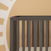 The Child Craft London 4-in-1 Convertible Crib in Dapper Gray, with baby-safe finishes and vertical slats, sits against a wall featuring a warm sunburst mural. A neutral mattress completes its modern look.