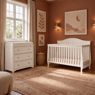 Child Craft Camden 2-Piece Nursery Set featuring a white convertible crib and a three-drawer dresser with a changing table topper in a nursery with terracotta walls and a patterned rug.