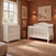 Child Craft Camden 2-Piece Nursery Set featuring a white convertible crib and a three-drawer dresser with a changing table topper in a nursery with terracotta walls and a patterned rug.