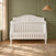 A matte white Child Craft Camden 4-in-1 Convertible Crib with a curved headboard and slatted sides, shown in a nursery.