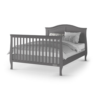 The Child Craft Camden 4-in-1 Convertible Crib in Cool Grey features a high slatted footboard and curved headboard, styled with white and gray bedding and pillows, shown against a plain white background.