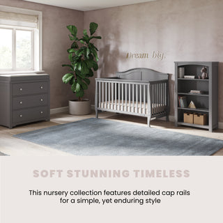 A soft-toned nursery features gray furniture, including the Child Craft Camden 4-in-1 Convertible Crib in Cool Grey, a dresser, and bookshelf, plus a potted plant and blue rug. "Dream big" is written on the wall. The look is soft, stunning, and timeless.